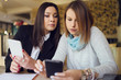 © Miljan Živković - Two young women female friends using smart phone smartphone at the restaurant cafe sitting by the table reading messages or browsing internet watching video or working shopping online