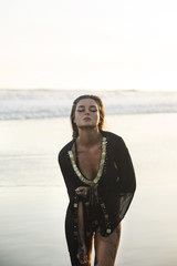 Wall Mural - Sexy woman wearing black tunic is posing on the beach with black sand