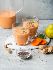 Wall Mural - Two glasses of fresh healthy carrot, pear, ginger smoothie with chia seeds on a grey background