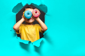 Happy cute boy is having fun played with donuts on black background wall.