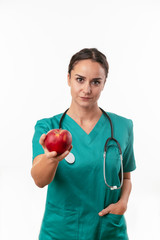 Wall Mural - Beautiful female doctor in green uniform. Portrait of nurse holding an apple. 