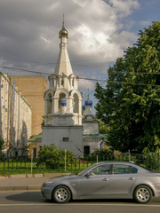 Wall Mural - On the opposite side of the road was a white stone openwork Church with blue domes against a background of Cumulus clouds and a gray car passing by