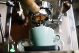 Fototapeta Mapy - Delicious fresh morning espresso coffee with beautiful crema puring through the bottomless portafilter with wooden handle into ceramic green cup