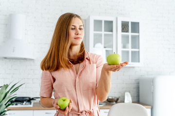 Canvas Print - Woman in kitchen ready to prepare meal with vegetables and fruits. Woman holding two apples in the kitchen background. Healthy food. Vegans. Vegeterian. concept