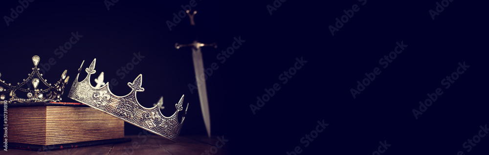 low key image of beautiful queen/king crown over antique book next to sword. fantasy medieval period. Selective focus - obrazy, fototapety, plakaty 