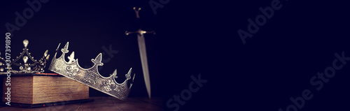 low key image of beautiful queen/king crown over antique book next to sword Tableau sur Toile