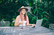 © BullRun - Cheerful woman in hat working and drinking coffee in garden
