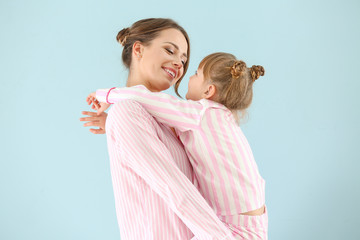 Portrait of happy mother and daughter in pajamas on color background