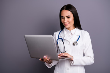 Portrait of concentrated successful brown hair doctor woman have patient consultation use computer read medical science information wear stethoscope white coat isolated grey color background