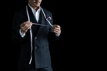 The dressmaker in black suit with Body measure tape was standing on a black background.