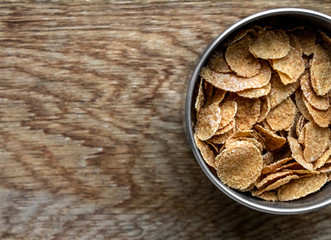 Wholemeal Cornflakes close-up in bowl on wooden background with copy space, useful breakfast whole grain corn flakes