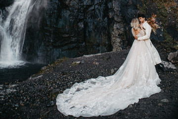 noise effect, selective focus: wedding couple model shoot, attractive bride in an incredibly beautiful long-flowing dress and groom in a waterfall background