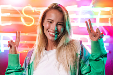 Poster - Image of woman showing peace fingers over multicolored neon text sign