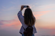 © Cavan Images - Young woman is taking a picture of the sky with her smartphone