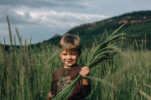 Little Boy Holding Grass In A Field Smiling
