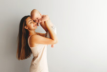 Beautiful Happy Mother Holds Her Baby On A Plain Light Background.