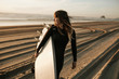 © Caleb Gaskins/Stocksy - Smiling woman with surfboard walking on beach during sunset