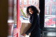 © jamie grill photography/Stocksy - Smiling woman holding package while standing at doorway