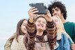 © guille Faingold/Stocksy - Happy teens friends embracing and taking selfie.