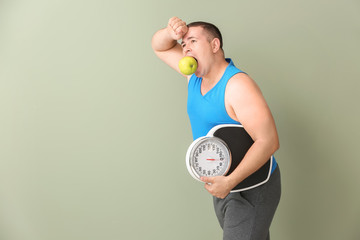 Sticker - Tired overweight man with scales and apple on color background. Diet concept