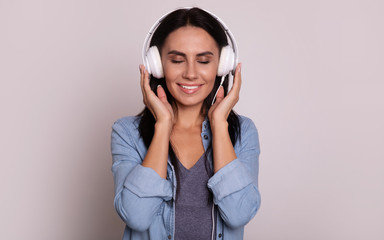 Listening carefully. Close-up photo of attractive woman in white headphones, who is listening to music with her eyes closed with joy and smiling broadly.