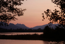 Scenic View Of Forggensee Lake And Silhouette Mountains Against Clear Sky During Sunset At Ostallg?u, Germany