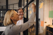 © Westend61 - Happy colleagues with sticky notes at glass pane in office