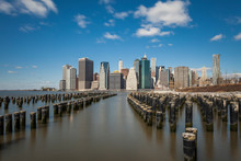 Wooden Posts In East River With Modern Buildings In Background Against Sky, New York City, USA