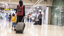 Back View Of Thai Young Muslim Mother Wearing Black Dress And Hijab Holding Suitcase With Her Son To Depart At The Airport.