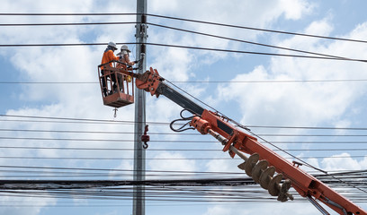 Two electrician workers are climbing on the electric poles to install and repair power lines.