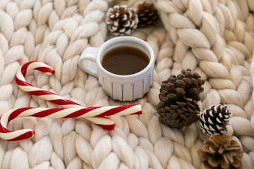 Coffee and candy canes on chunky knit blanket styled with pine cones, cozy Christmas photo