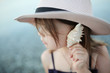 child in swimsuit and hat listens to sea in shell