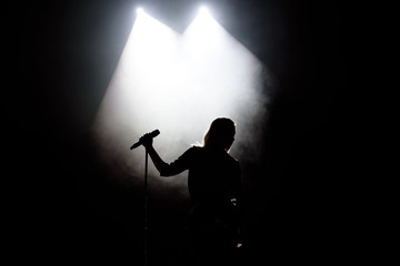 black silhouette of female singer with white spotlights in the background