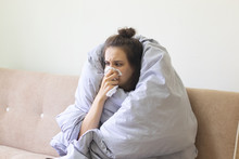 Sick Young Woman In Blanket Sits At Home With A Runny Nose.
