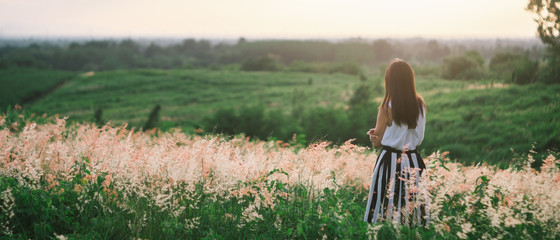 Wall Mural - Trendy girl in stylish summer dress feeling free in the field with flowers in sunshine.