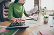 Cropped closeup photo of busy business lady notebook table hold paper stats calculating numbers sums money income sit chair wear green turtleneck modern office