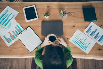 High angle above view photo of pretty business lady holding hot drink mug look paper sheets company money income sit chair wear green turtleneck office room indoors