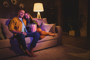 Nice attractive lovely cheerful cheery couple girl sitting on divan enjoying snack watching film spending day weekend holiday at night dark home house apartment indoors