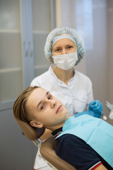 Teen guy patient sitting in a chair and woman dentist, together portrait in dental room.