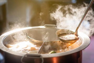 Cooking person in the restaurant is cooking while using the dipper in a large soup pot. And the water is boiling, there is smoke and hot spit.