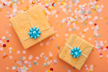  top view of blue bows on gift boxes near confetti on orange