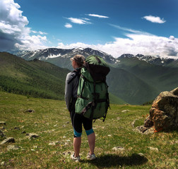 A young woman traveler with a backpack looks at the distance at a beautiful mountain range.