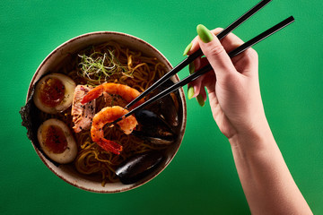 Wall Mural - cropped view of woman eating spicy seafood ramen with chopsticks on green surface