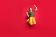 Full size photo of excited millennial lady jumping high cheerful mood rejoicing celebrating victory wear casual yellow trousers green t-shirt isolated red color background