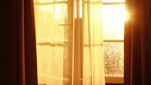 Sunbeams Through Transparent Curtain Of Opened Window At The Time Of Beautiful Red Sunset With The Light Breeze