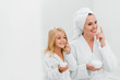 © LIGHTFIELD STUDIOS - cheerful mother and daughter applying cosmetic cream in bathroom