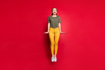 Poster - Full body photo of crazy youngster lady jumping high spending best free time excited cheerful mood wear casual yellow trousers green t-shirt isolated red color background