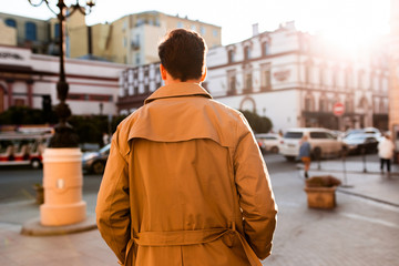 Back view of young stylish man in trench coat walking through street