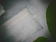 An Empty Gritty Cold Urban Inner City Basketball Court, Photographed From Above. Drone Photography Showing Court Lines, Tennis Court And A Concrete Basketball Court. Atmospheric Overhead Viewpoint.
