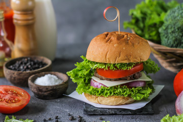 Photo of fresh burger on wooden cutting board on dark background..Homemade hamburger with beef, onion, tomato, lettuce and cheese. Homemade fast food. Dark textured background. Copy space. Image.